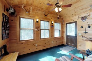 A cabin interior with wooden walls, large windows, a ceiling fan, and mounted antlers. - Lakefront Cabin with Lake Views, Cable, Beach Access & Private Dock (Greenville)