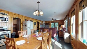 A wooden interior with a dining table, chairs, a kitchen area with appliances, and a sofa.