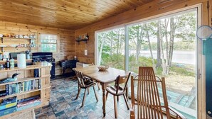 A wooden cabin interior with a dining area, kitchen, and large windows.
