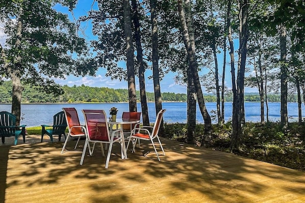 A deck with outdoor seating, a table, and chairs overlooking a lake.
