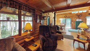 A log cabin interior with a fireplace, seating area, and large windows. - Dog-Friendly Lakefront Log Cabin with Peaceful Atmosphere, Dock & Boat Launch (Rockwood)