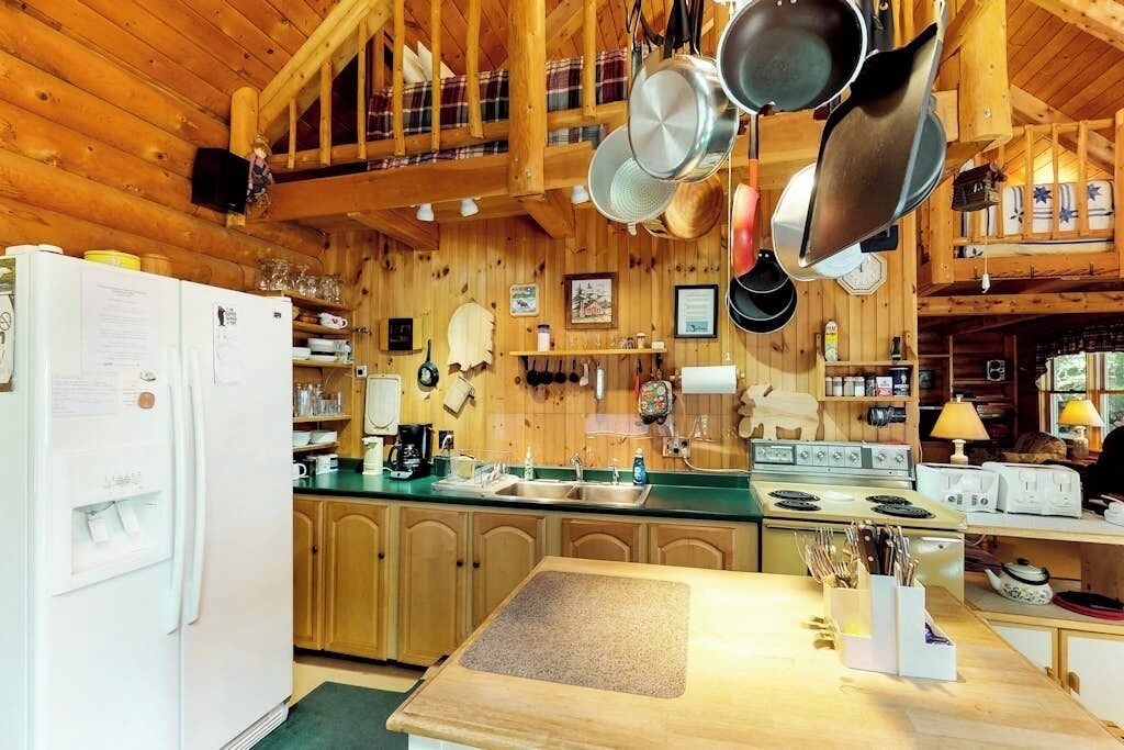 A wooden cabin kitchen with a refrigerator, sink, stove, and hanging pots.