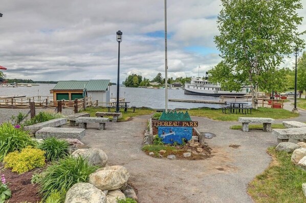 Entrada a un parque con un letrero, un muelle, un bote y un edificio con techo verde.