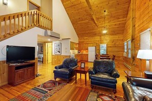 A spacious living area with a wooden ceiling, a television, leather sofas, and a staircase. - Scenic dog-friendly cabin with kitchen, AC, firepit, WiFi & nearby hiking (Northport)