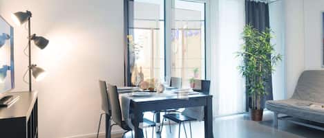 A modern living room with a dining table, chairs, a sofa, a large window, and a potted plant.