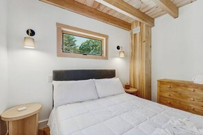 A bedroom with a bed, bedside tables, a window, and wooden walls. - Spruce Shores Retreat: New Home with Hot Tub, Spacious Deck, Gas Grill, WiFi, and Washer/Dryer (Boothbay)