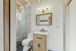 A bathroom with a toilet, sink, mirror, and shower. - Spruce Shores Retreat: New Home with Hot Tub, Spacious Deck, Gas Grill, WiFi, and Washer/Dryer (Boothbay)