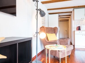 Ein gemütliches Wohnzimmer mit einem braunen Sessel, einem kleinen runden Tisch mit Zeitschriften, einer Stehlampe und einer Küchenzeile im Hintergrund.