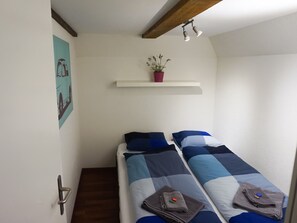 Ein Zimmer mit zwei Betten, einer kleinen Ablage mit einer Pflanze und einer Tür mit Griff.