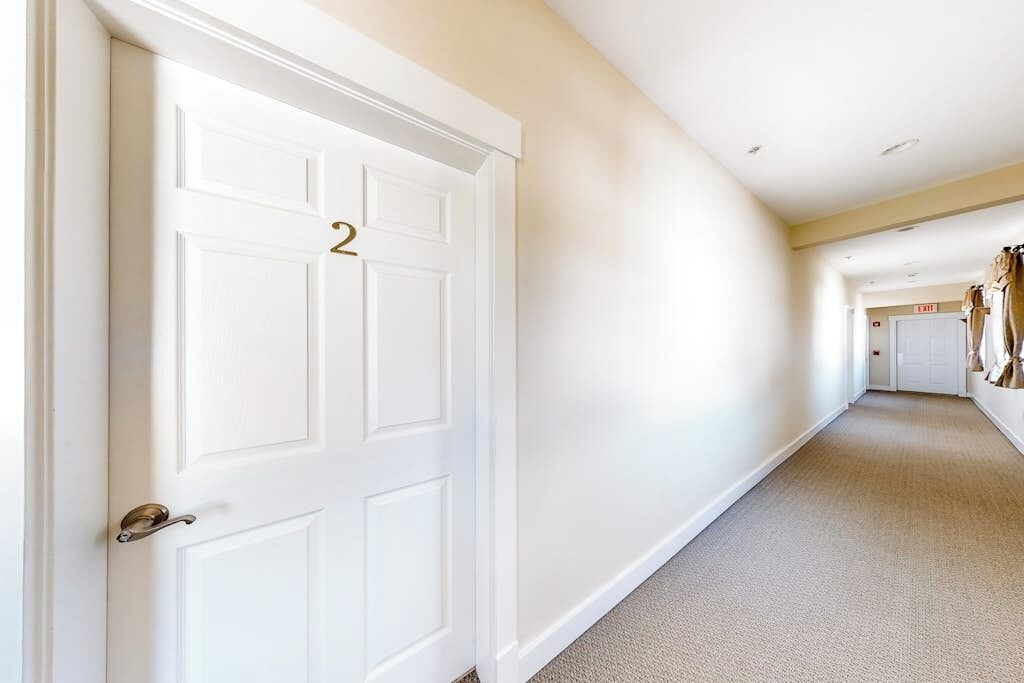 A hallway with a white door marked with the number 2, carpeted flooring, and a plain wall.