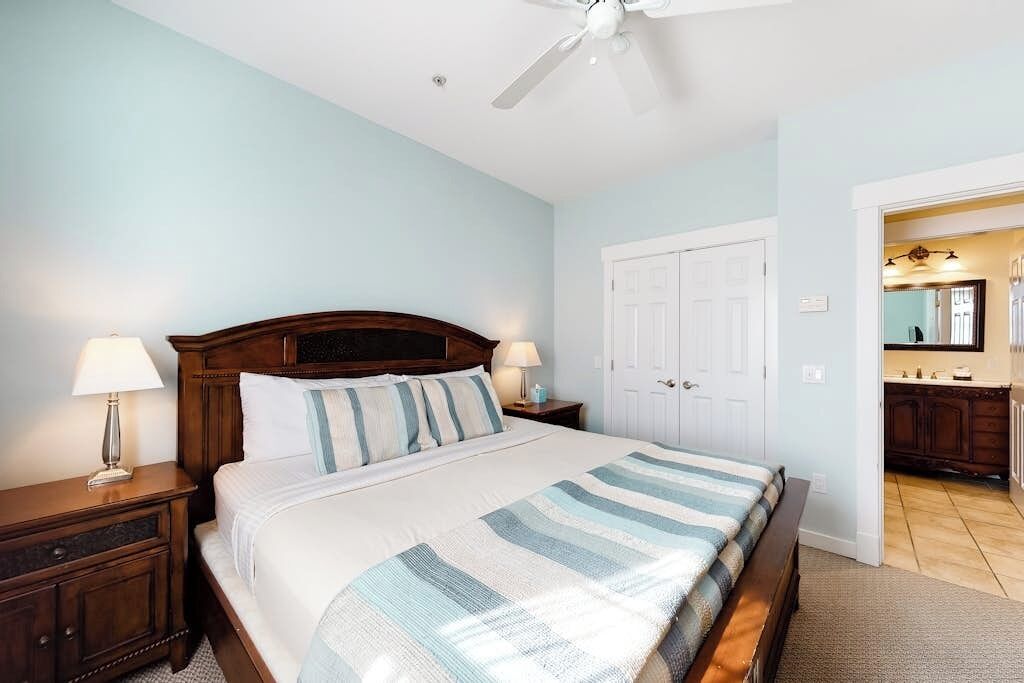 A bedroom with a bed, nightstands, a ceiling fan, a door, and a bathroom visible through an open doorway.
