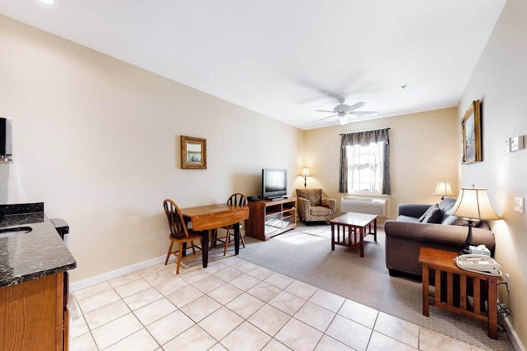A living room with a dining table, a sofa, a TV, and a ceiling fan.