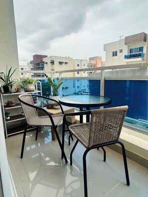 A balcony with a round table and two wicker chairs, overlooking a swimming pool and adjacent buildings. - 2-bedrooms apartment in peaceful Concepción La Vega with AC (Concepción La Vega)