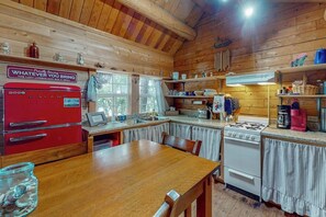 A wooden cabin interior with a kitchen, dining table, and a red appliance.