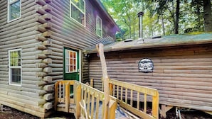 Een vakantiehuisje van hout met een groene deur, een houten trap en een bordje dat aangeeft dat het een camping is.