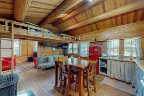 Interior d'una cabana de fusta amb zona de menjador, cuina i espais al pis superior per dormir.