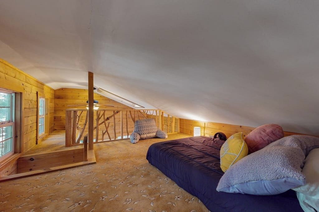 Een slaapkamer met een schuine kap, houten wanden, een bed met kussens en een raam.