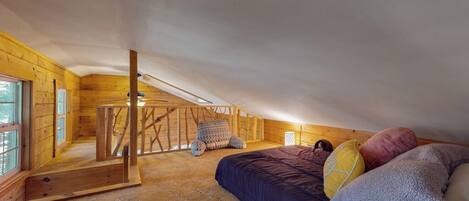 Een slaapkamer met een schuine kap, houten wanden, een bed met kussens en een raam.