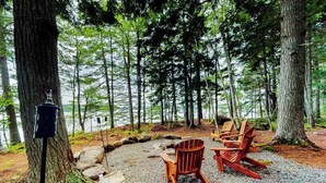 A forested area with a gravel path, wooden Adirondack chairs, and a bird feeder. - 2 beautifully designed, off-the-grid homes with amazing lakefront views & access (Franklin)