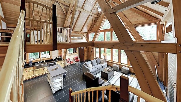 A spacious loft-style room with a high ceiling, large windows, a fireplace, and a cozy seating area. - 2 beautifully designed, off-the-grid homes with amazing lakefront views & access (Franklin)