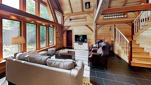 A spacious living room with a large sofa, a television, and a staircase. - 2 beautifully designed, off-the-grid homes with amazing lakefront views & access (Franklin)