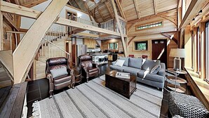 A spacious loft-style living area with a high ceiling, wooden beams, a staircase, a sofa, leather chairs, and a dining area. - 2 beautifully designed, off-the-grid homes with amazing lakefront views & access (Franklin)