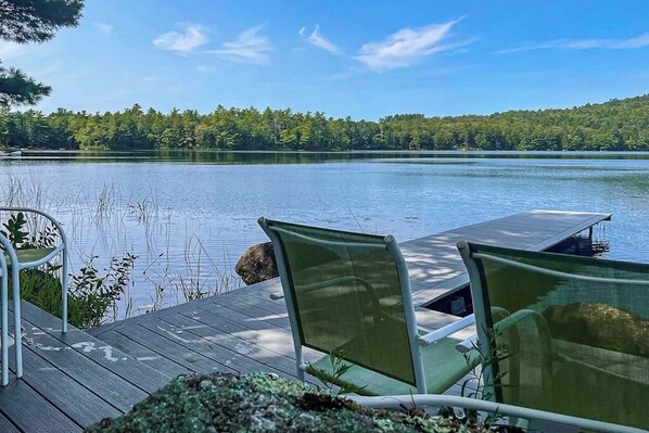 A wooden deck with two green chairs facing a calm lake, surrounded by trees. - Secluded waterfront home with private dock, outdoor dining, firepit, WiFi & W/D (Orland)