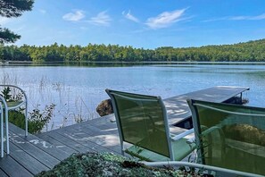 Une terrasse en bois avec deux chaises vertes, donnant sur un lac paisible, le tout entouré d’arbres.