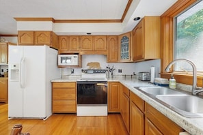 A kitchen with wooden cabinets, a white refrigerator, a stove, a microwave, and a sink. - Secluded waterfront home with private dock, outdoor dining, firepit, WiFi & W/D (Orland)