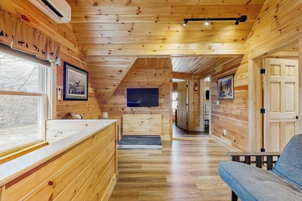 A wooden interior with a bench, a television, and a hallway leading to a door.