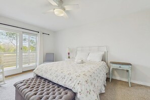 A bedroom with a bed, a nightstand, a bench, a ceiling fan, and a window with a view. - Modern farmhouse with deck, firepit, & balcony (Northport)