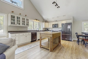 A kitchen with white cabinets, a wooden island, stainless steel appliances, and a dining area with chairs. - Modern farmhouse with deck, firepit, & balcony (Northport)
