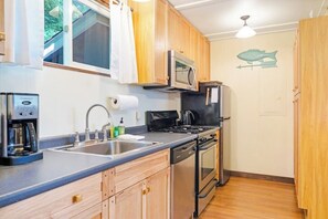 Una cucina compatta con forno a microonde, piano cottura e lavastoviglie, mobili in legno e una finestra con tende.