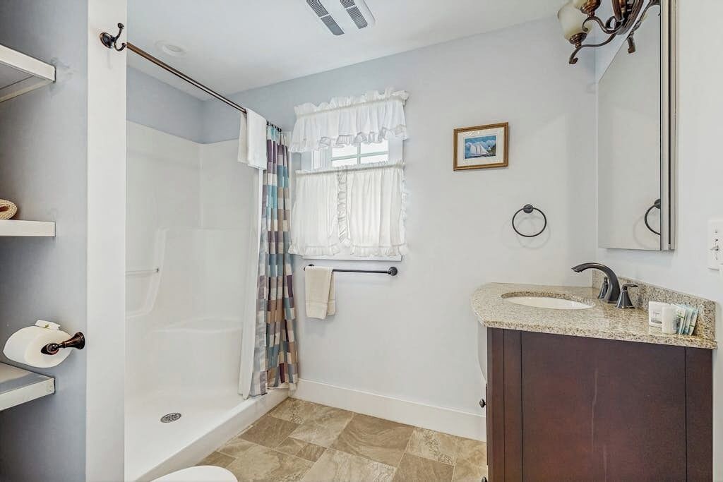 Een badkamer met douche, toilet, wastafel en een raam met gordijnen.