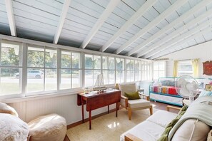A room with a high ceiling, large windows, a wooden desk, a sofa, and a bed with a colorful blanket. - Charming Boothbay Harbor cottage with partial AC, full kitchen, and sun room (Boothbay Harbor)