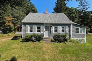 A single-story house with a gray shingled roof, white trim, and a front door. - Charming Boothbay Harbor cottage with partial AC, full kitchen, and sun room (Boothbay Harbor)