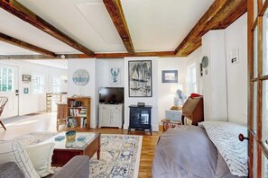 A room with a wooden ceiling, a bed, a TV, a bookshelf, and a fireplace. - Charming Boothbay Harbor cottage with partial AC, full kitchen, and sun room (Boothbay Harbor)