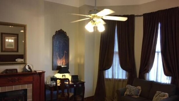 A room with a fireplace, a ceiling fan, a sofa, and a window with curtains. - 1896 O'Malley House (New Orleans)