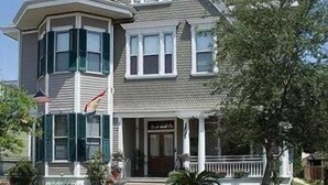 A two-story house with a gabled roof, a front porch, and a flag. - 1896 O'Malley House (New Orleans)