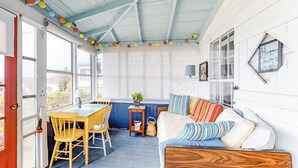 A cozy room with a wooden ceiling, a dining table with chairs, a sofa with striped cushions, and a window with curtains. - Ocean Point Cottage- large porch, ocean view, water access (East Boothbay)