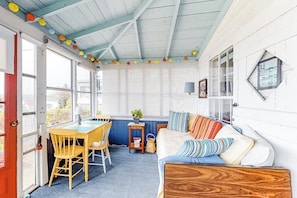 Ein gemütliches Zimmer mit Holzbalkendecke, einem Esstisch mit Stühlen, einer Couch mit gestreiften Kissen und einem Fenster mit Vorhängen.