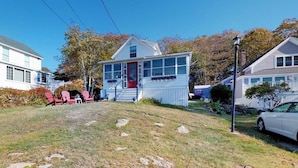 A residential house with a front porch, a garage, and a lawn with rocks. - Ocean Point Cottage- large porch, ocean view, water access (East Boothbay)