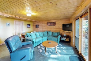 A cozy room with a wooden ceiling, a blue sofa, a round coffee table, and a television. - Waterfront cabin w/ outdoor firepit, dock, and lake views - dogs welcome (Greenville)
