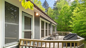Une terrasse en bois avec un barbecue, une table et des chaises, le tout entouré d’une rambarde en bois.