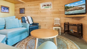 L’intérieur d’un chalet accueillant, avec un canapé, une petite table, un téléviseur fixé au mur et une fenêtre donnant sur le paysage extérieur.