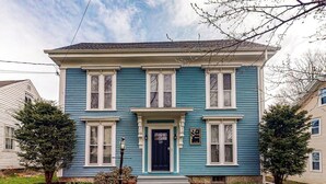 Una casa de dos pisos con fachada azul oscuro, detalles blancos y una puerta principal negra.