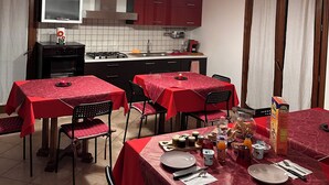 A dining area with red tablecloths, chairs, and a kitchen in the background.