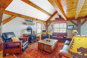 A cozy loft-style living room with a fireplace, leather furniture, and a rustic ceiling. - Spectacular lakefront home with dock, firepit, & vaulted ceilings - dog-friendly (Greenville)