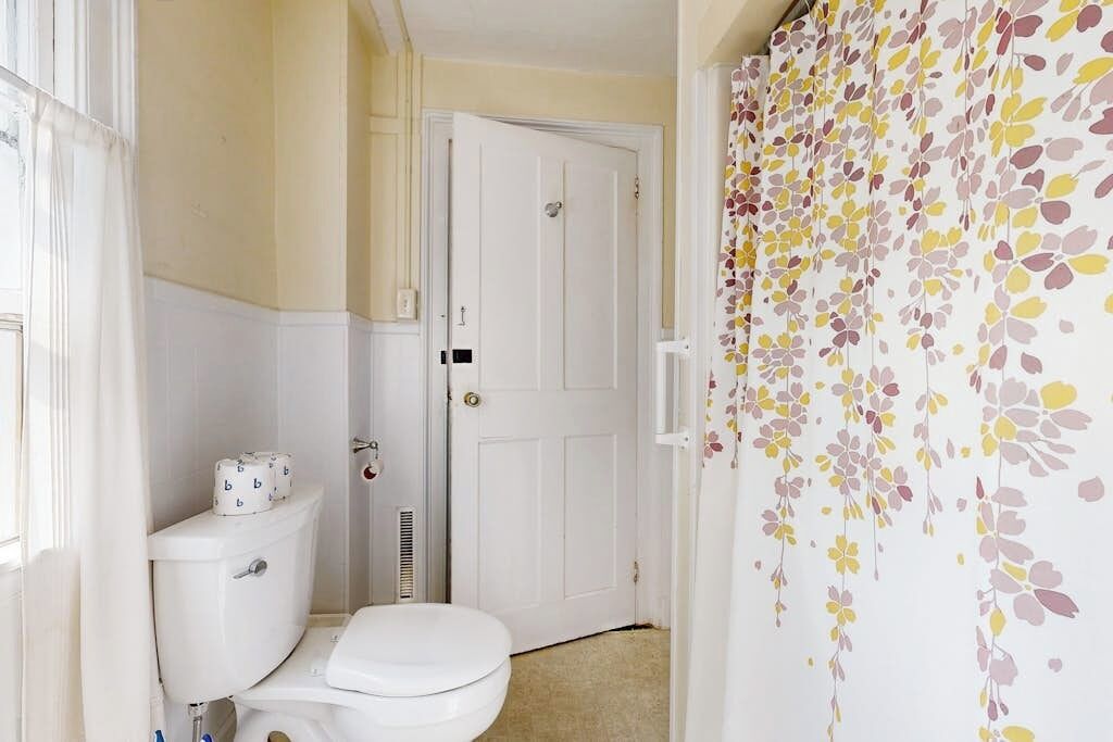Ein Badezimmer mit Toilette, einer weißen Tür und einem Duschvorhang mit Blumenmuster.