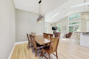 Un'ampia sala da pranzo con tavolo e sedie in legno, un lampadario e grandi finestre che lasciano entrare la luce naturale.
